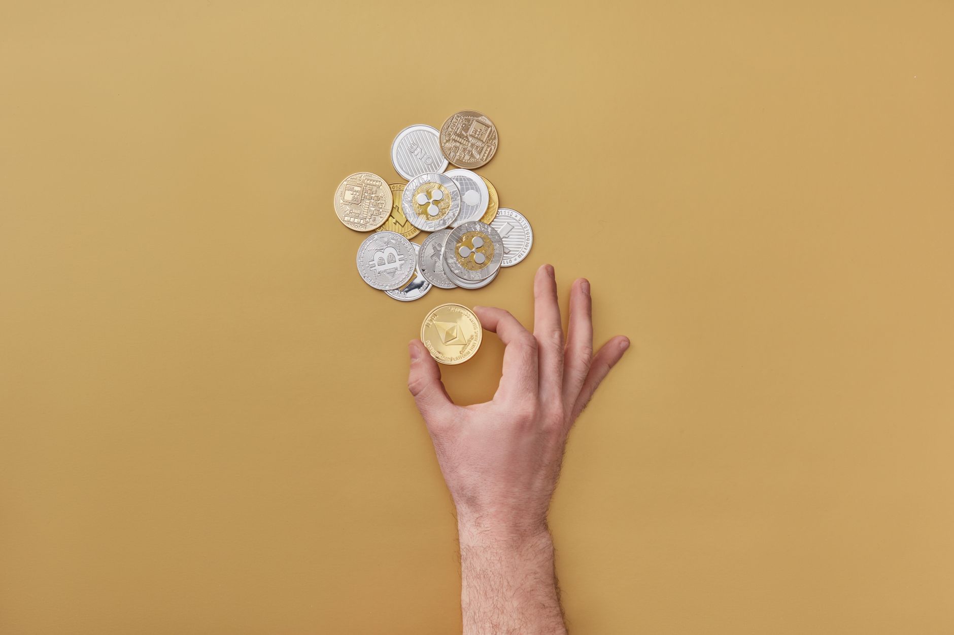 Hand holding coins with various cryptocurrencies on a yellow background. Perfect for finance-themed designs.